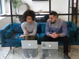 A man and woman sitting on a couch with their laptops.